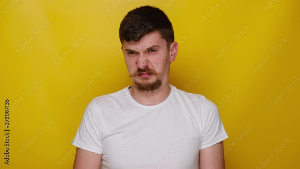 Young man squeezing nose with fingers, smells something awful, looking in camera with disgust expression, wears white t-shirt, feeling bad about bad smell, isolated on yellow studio background Young man squeezing nose with fingers, smells something awful, looking in camera with disgust expression, wears white t-shirt, feeling bad about bad smell, isolated on yellow studio background