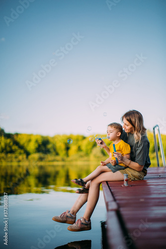 Fototapeta Cool mother and baby boy sitting on dock launch soap bubbles