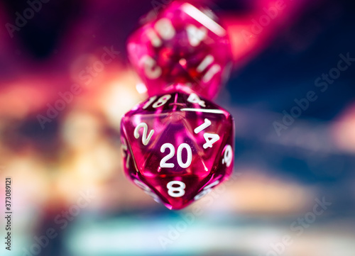Close up of a transparent pink polyhedral dice against a blurry colorful background. D20