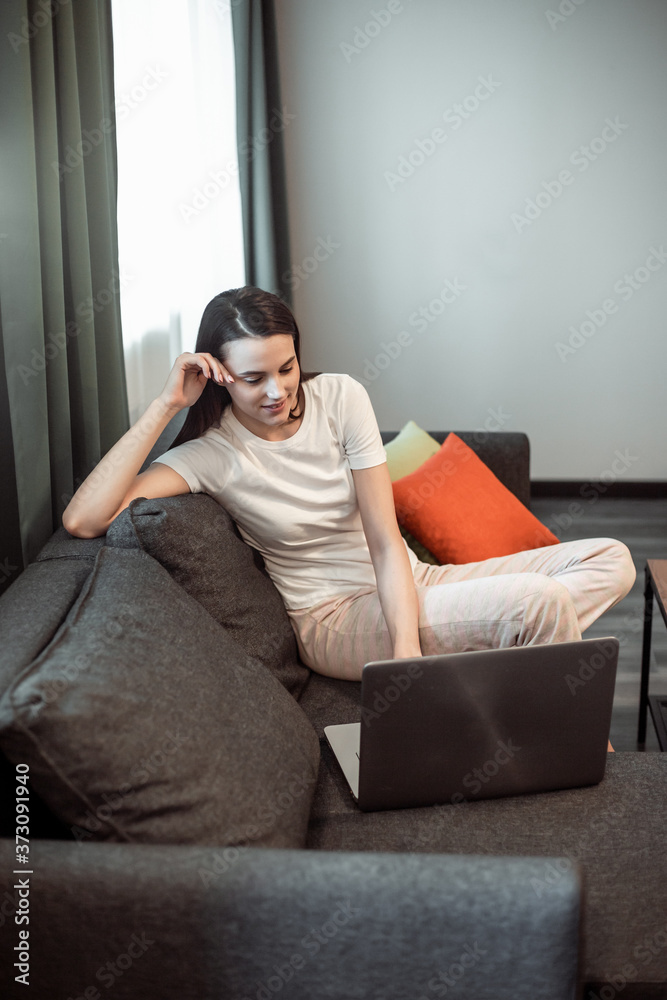 Young woman with modern laptop sitting on sofa at home