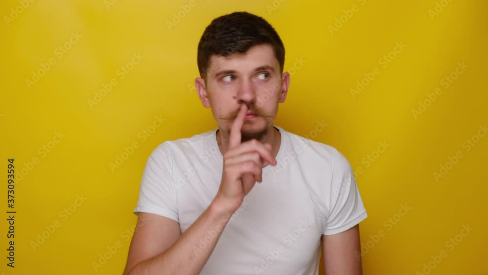 Portrait of young man shushing with finger on lips gesture, asking to keep silence and looking at camera with serious expression, isolated on yellow background, mysterious confidential information Portrait of young man shushing with finger on lips gesture, asking to keep silence and looking at camera with serious expression, isolated on yellow background, mysterious confidential information