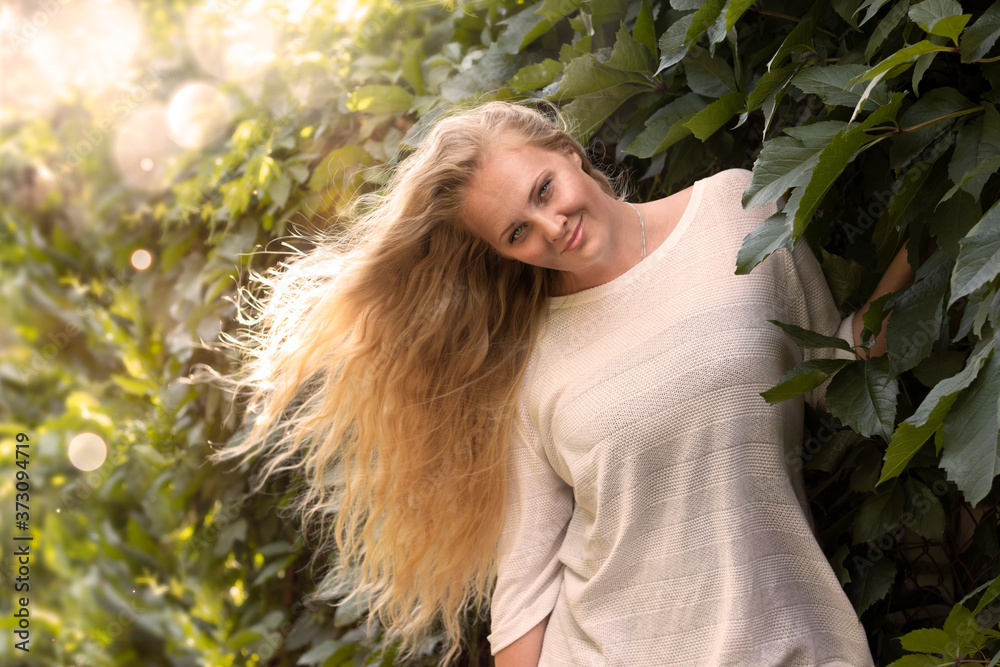 Happy, beautiful young blonde with long hair in a white dress on a background of green leaves. Happy, beautiful young blonde with long hair in a white dress on a background of green leaves.