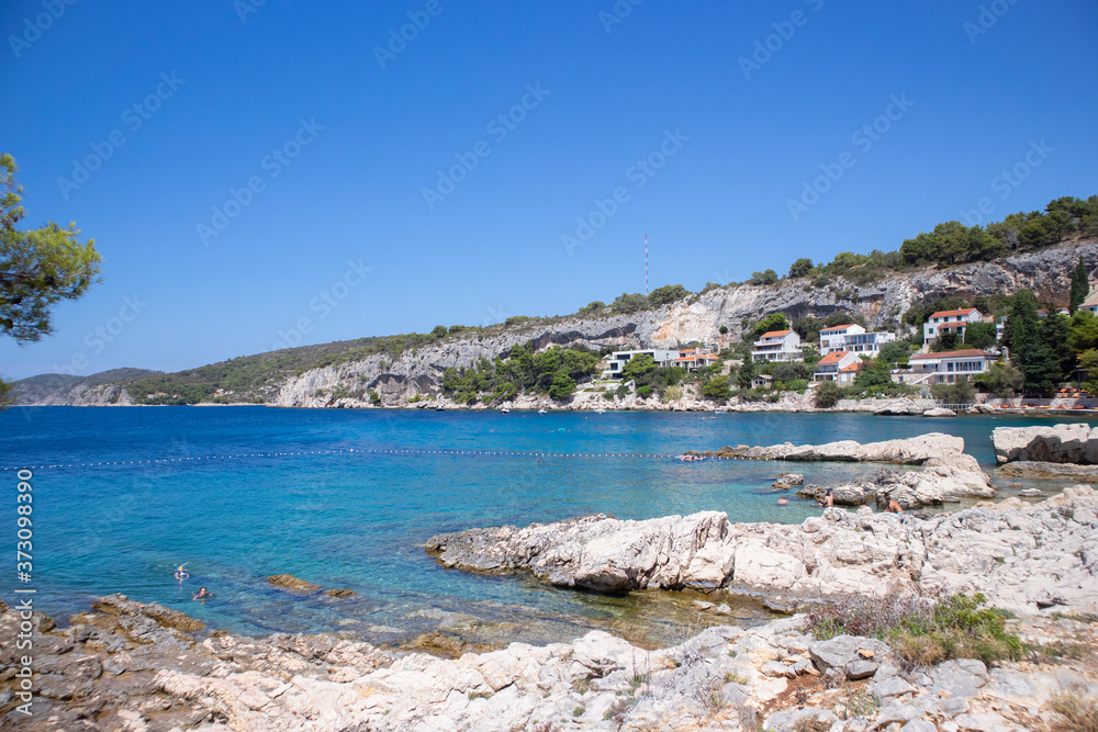 Beautiful rocky beach and steep cliffs at Hvar island, Croatia, towering above turquoise sea water