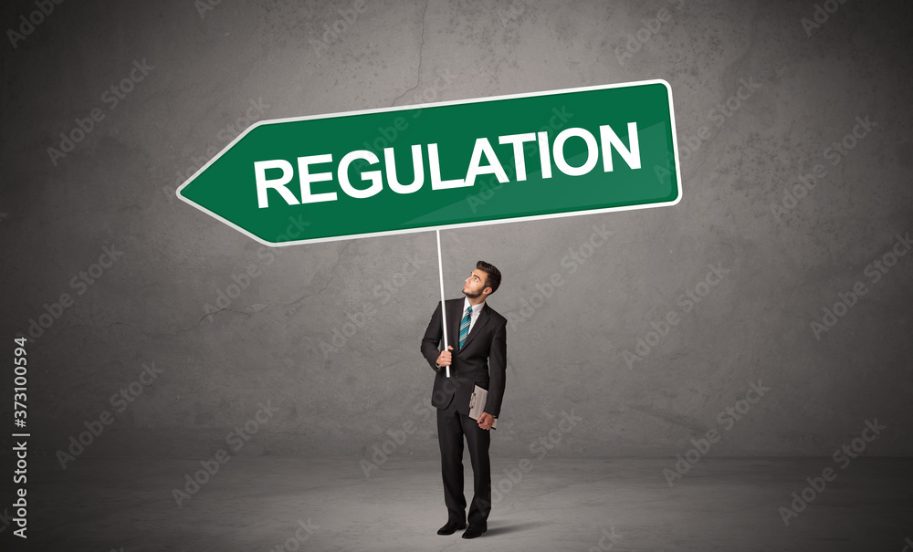 Young business person in casual holding road sign with REGULATION inscription, new business direction concept Young business person in casual holding road sign with REGULATION inscription, new business direction concept