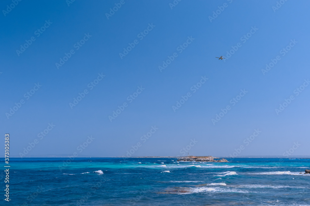 Seascape with beautiful blue sea and white waves in the distance lighthouse, seaplane in the air flies to the island of Formentera. Ibiza. Balearic Islands, Spain