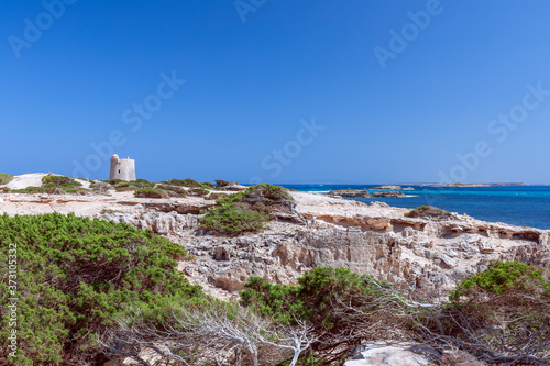 Beautiful view of the old observation tower (Torre De Ses Portes) and the rocky coast of the Ibiza island.
