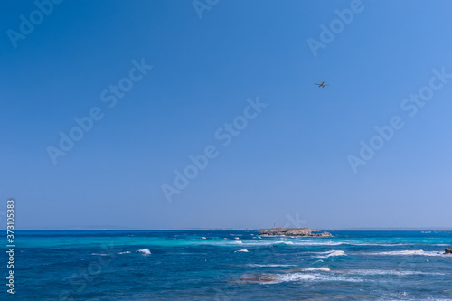 Seascape with beautiful blue sea and white waves in the distance lighthouse, seaplane in the air flies to the island of Formentera. Ibiza. Balearic Islands, Spain