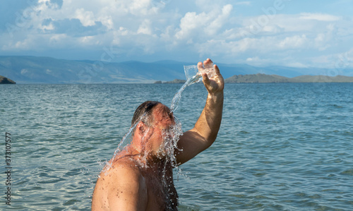 man douses himself with clean water from a Cup on the lake photo