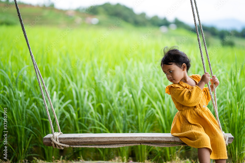 Cute little girl sitting at wooden swing against rice terrace field.