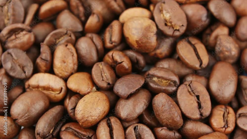 Close-up of the rotation of coffee beans. Roasted grains of aromatic coffee rotate on a plate. Close-up of the rotation of coffee beans. Roasted grains of aromatic coffee rotate on a plate.
