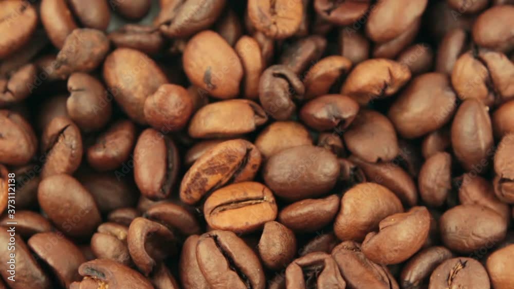 Close-up of the rotation of coffee beans. Roasted grains of aromatic coffee rotate on a plate. Close-up of the rotation of coffee beans. Roasted grains of aromatic coffee rotate on a plate.