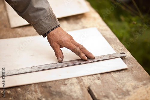 Senior elderly carpenter using a straightedge to draw a line on a board.