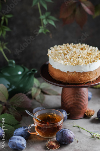 Cake with sour cream and almond flakes on a high stand. Autumn still life with tea and pie. Decor from natural materials.