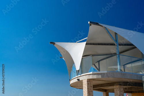 white veranda with fabric roof against blue sky.