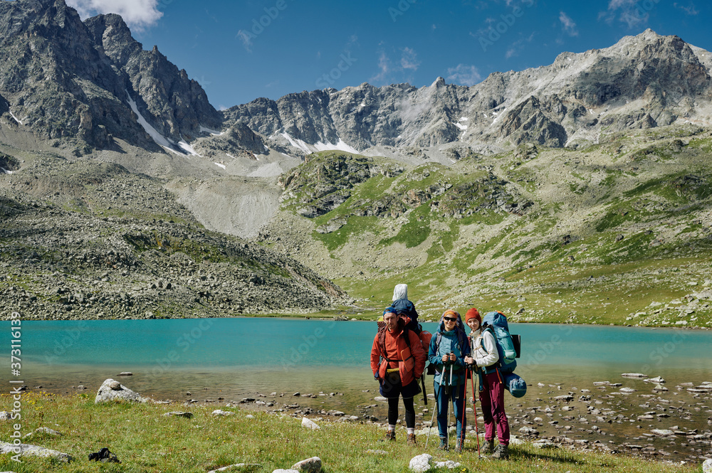 Three hikers friends - one man and two women are staying by the turquoise lake among mountains. Extreme tourists in wild nature landscape. Domestic travel trekking lifestyle. Local tourism
