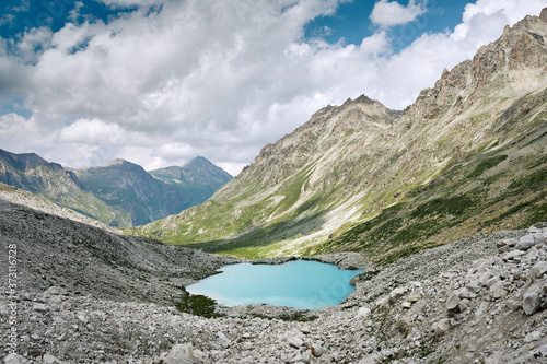 Turquoise mountain lake among rocky hills. Majestic wild nature landscape of mountain ranges, blue lake and cloudy sky.