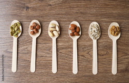 Some of the assorted nuts with pistachios, almonds, pumpkin seeds, sunflower seeds, hazelnuts in wooden spoons on a wooden background, top view.