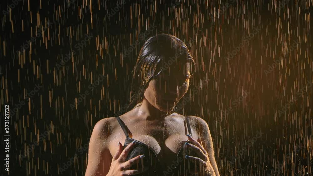 Sexy woman's wet shapes. Woman posing naked in her underwear under pouring rain. Silhouette of a beautiful body on a black background. Silhouette. Close up. Slow motion.