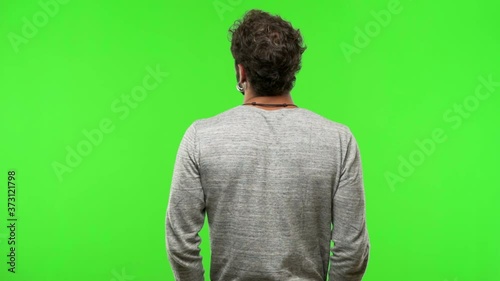 young man on chroma green screen from behind, looking back