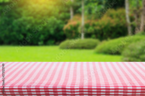 Red checkered tablecloth texture top view with abstract green bokeh from garden in morning background.For montage product display or design key visual layout and summer season.