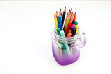 Artist's set. Colored pencils and markers lie in a beautiful purple translucent jar on a white background