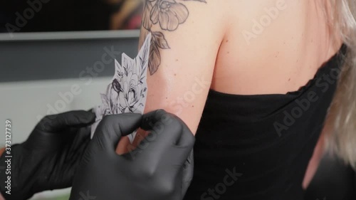 The tattooist glues a tattoo stencil to a girl's arm.