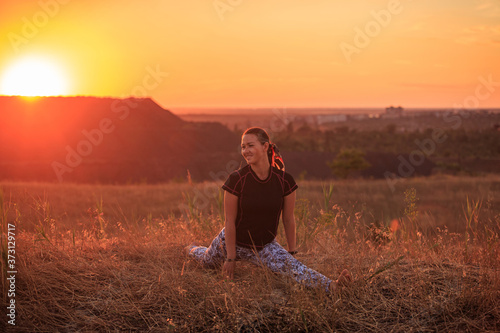 Girl practices yoga on a hill in nature during sunset or dawn