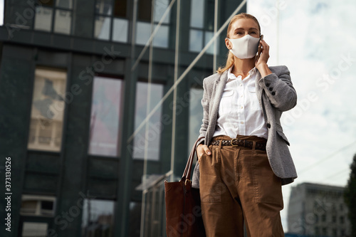 Business during covid 19. Confident business woman wearing protective face mask talking on mobile phone while standing against office building outdoors