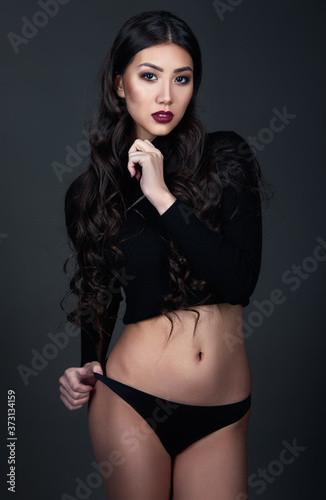 Studio fashion shot of pretty young woman. Portrait of beautiful girl dressed in black panties and jersey. Seductive lady against gray background