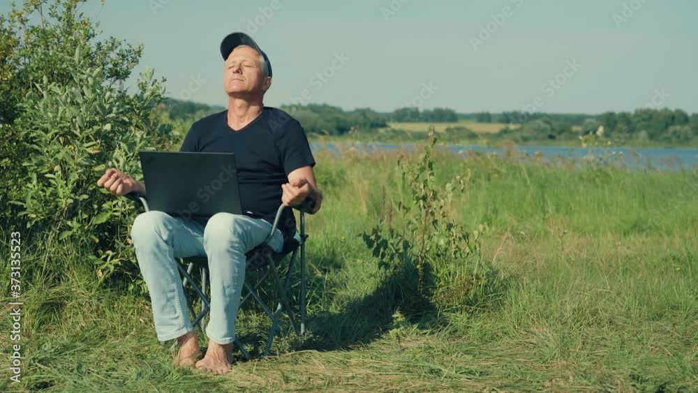 A man works at a computer sitting on a chair in nature. A man works at a computer sitting on a chair in nature.