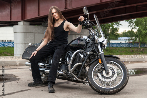 Long-haired guy on a black motorcycle under the bridge