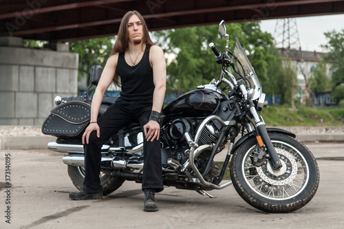 Long-haired guy on a black motorcycle under the bridge