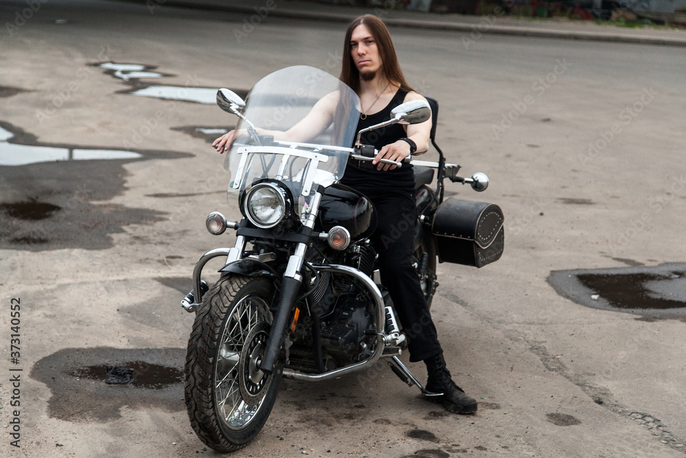 Obraz premium Long-haired guy on a black motorcycle under the bridge