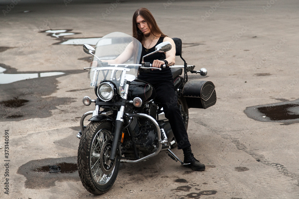 Obraz premium Long-haired guy on a black motorcycle under the bridge