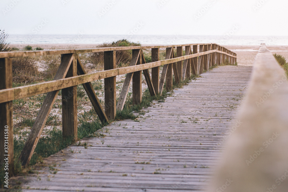 Wooden path at Atlantic Ocean over sand dunes with ocean view, sunset summer evening.