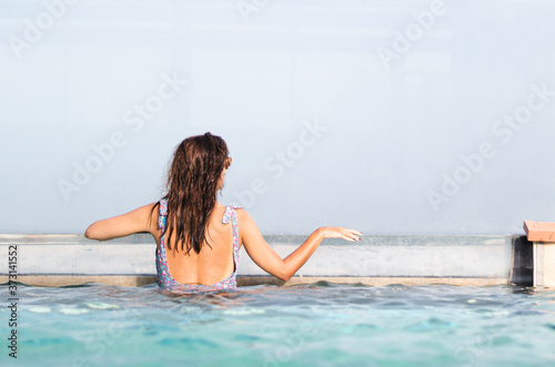Nice young woman in a flowered bathing suit leaning against the edge of the pool looking out over the horizon.
