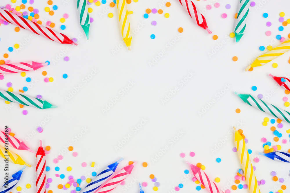 Colorful birthday cake candles with candy sprinkles. Top down view frame on a white background. Copy space.