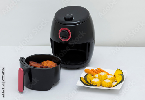 Air fryer machine with chicken and vegetables on white background