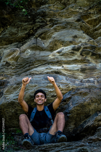 Young boy showing thumbs up into the camera from a height  after climbing a huge rock.