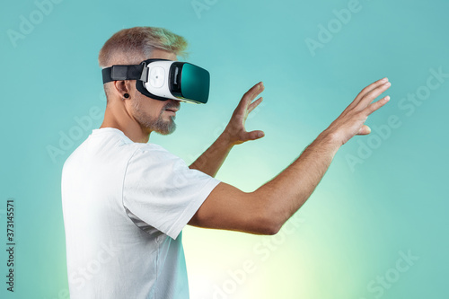 Suprised bearded hipster man with blonde hair wearing virtual reality goggles in studio in neon lights.