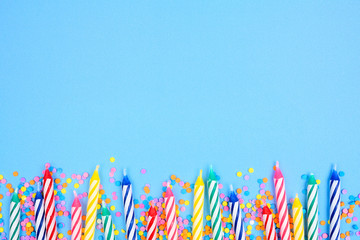 Birthday cake candles with candy sprinkles. Above view bottom border on a blue background. Copy space.