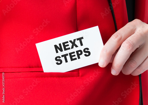 Closeup on businessman holding a card with text NEXT STEPS, business concept image with soft focus background