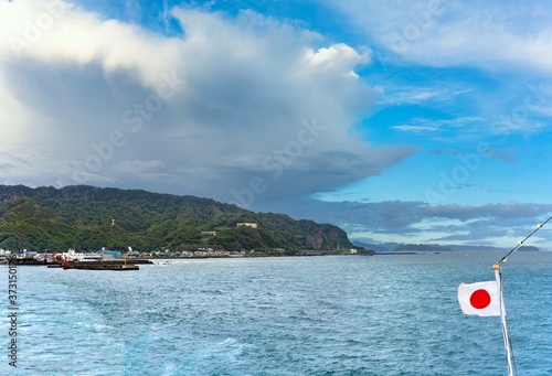 Coast of the Kanaya Port Ferry Terminal from the kanayamaru with a japanese national flag waving along the Uraga Channel with the cliffs of the Mount Nokogiri stone quarry photo