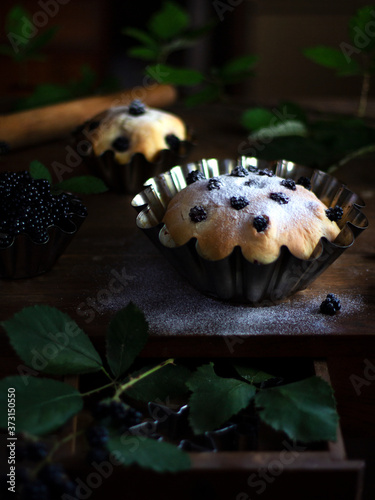 Delicious delicious pastries with berries on a vintage brown table with green BlackBerry branches. An open mailbox with a creative solution. Berry cupcake sprinkled with powdered sugar. Dark mood
