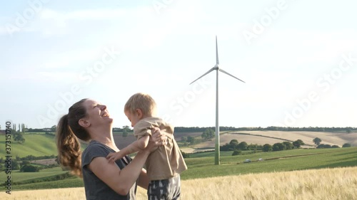 Happy mother plays with her son in a field with a wind turbine in the background on a beautiful summer day