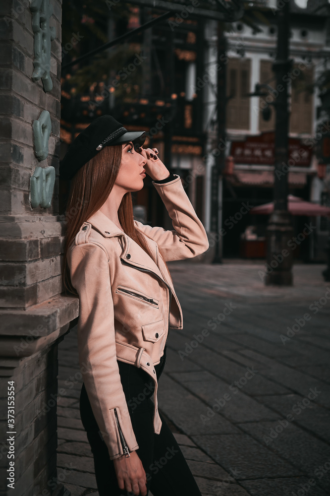 Fototapeta premium beautiful model in a black hat and beige jacket poses near a lamppost . city background 