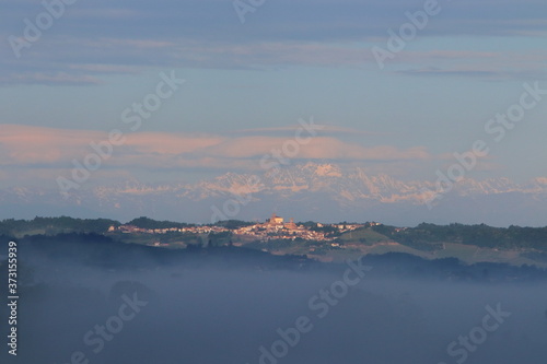 A view of the Monferrato Astigiano hills shrouded in thick fog with the snowy Alps in the background.