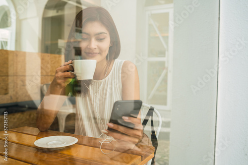 Young latin woman using phone at coffee shop. photo