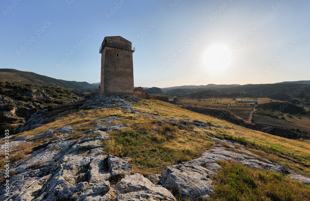 In the Spanish province of Castilla. The old tower of the Castillo Taibailla with the sunset in the backlight. In the foreground are stones and grass.