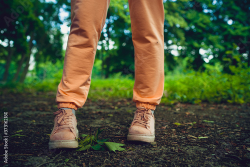 Close up of woman's feet in shoes on ground. Woman in pink sneakers stands in park in summertime.
